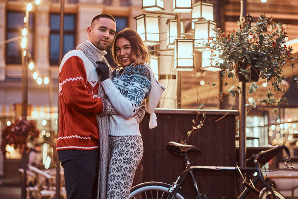 A young romantic couple wearing warm clothes hugging outdoor in evening street at Christmas time, enjoying spending time together. - Foto, Imagen