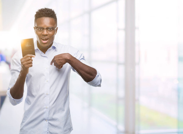 Νεαρός αφρικανική αμερικανική άνθρωπος που κρατά αυστραλιανό διαβατήριο με προτεταμένο δάχτυλο πρόσωπο έκπληξη για τον εαυτό του - Φωτογραφία, εικόνα