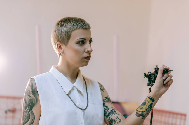Young female tattoo master threateningly holding small apparat - Фото, зображення