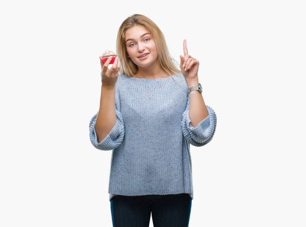 Young caucasian woman eating sweet cupcake over isolated background surprised with an idea or question pointing finger with happy face, number one - Фото, зображення