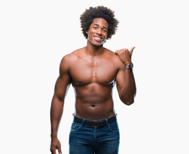 Hombre afroamericano sin camisa mostrando cuerpo desnudo sobre fondo aislado sonriendo con cara feliz mirando y señalando hacia un lado con el pulgar hacia arriba
. - Foto, imagen