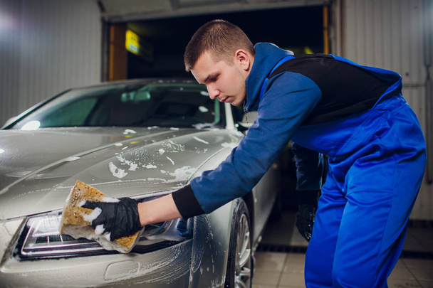 outdoor car wash with yellow sponge. Beautiful man washes car - 写真・画像