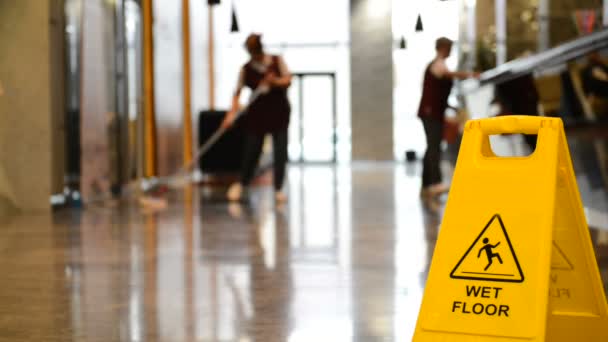 Yellow warning sign wet floor. Sign showing warning of caution wet floor and workerw cleaning hall floor of  business building. - Footage, Video