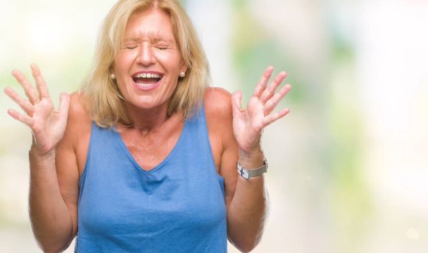 Middle age blonde woman over isolated background celebrating mad and crazy for success with arms raised and closed eyes screaming excited. Winner concept - Fotoğraf, Görsel