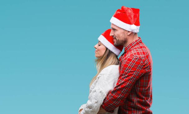 Молодая пара влюбленных носить рождественскую шляпу на изолированном фоне глядя в сторону, расслабиться профиль позировать с естественным лицом с уверенной улыбкой
. - Фото, изображение