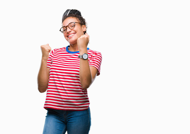Young gevlochten hair Afrikaans Amerikaans meisje bril over geïsoleerde achtergrond erg blij en opgewonden doet winnaar gebaar met armen naar voren gebracht, glimlachend en schreeuwen voor succes. Viering concept. - Foto, afbeelding