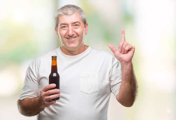 Красивый пожилой человек пьет бутылку пива на изолированном фоне, удивленный идеей или вопросом, указывая пальцем со счастливым лицом, номер один
 - Фото, изображение