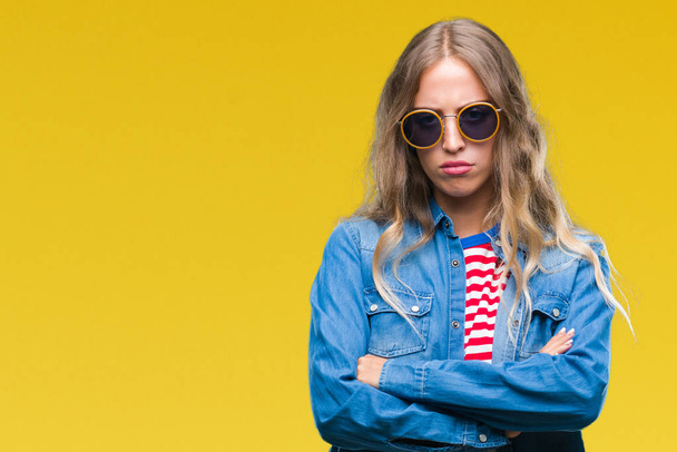 Beautiful young blonde woman wearing sunglasses over isolated background skeptic and nervous, disapproving expression on face with crossed arms. Negative person. - Valokuva, kuva
