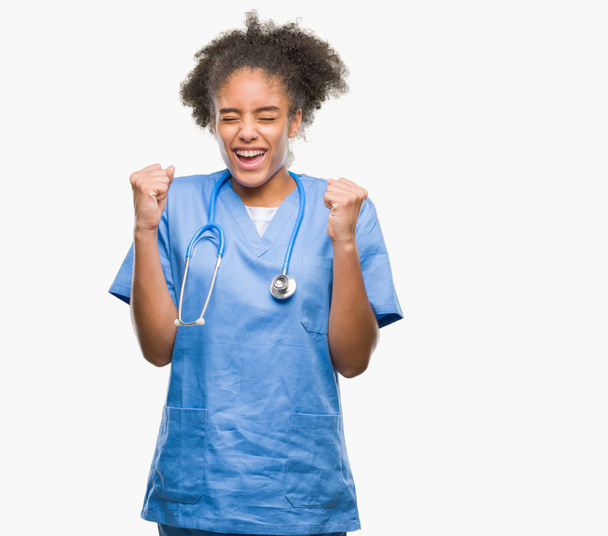 Jeune afro-américaine médecin femme sur fond isolé excité pour le succès avec les bras levés célébrer la victoire en souriant. Concept gagnant
. - Photo, image