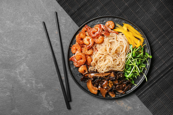 Тарелка с вкусной китайской лапшой, креветки и овощи на столе, вид сверху
 - Фото, изображение