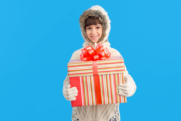 Little girl in winter clothes with a big gift box in hands on a blue background. Christmas presents. - Photo, image