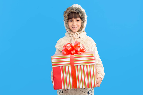 Little girl in winter clothes with a big gift box in hands on a blue background. Christmas presents. - Фото, зображення