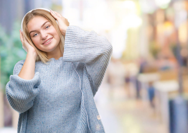Mujer caucásica joven escuchando música con auriculares sobre un fondo aislado con una sonrisa alegre y fresca en la cara. Persona afortunada
. - Foto, Imagen