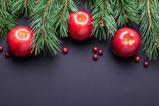 Christmas background with tree branches, red apples and cranberries. Dark wooden table. Top view. Copy space - Photo, image