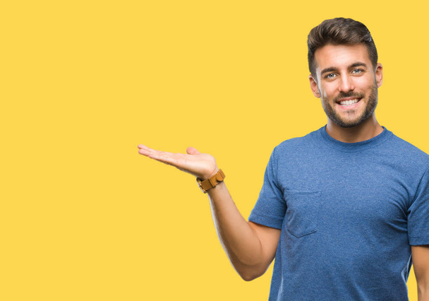 Young handsome man over isolated background smiling cheerful presenting and pointing with palm of hand looking at the camera. - Photo, Image