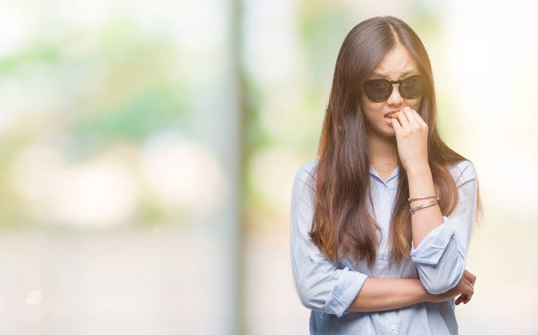 Young asian woman wearing sunglasses over isolated background looking stressed and nervous with hands on mouth biting nails. Anxiety problem. - Foto, afbeelding