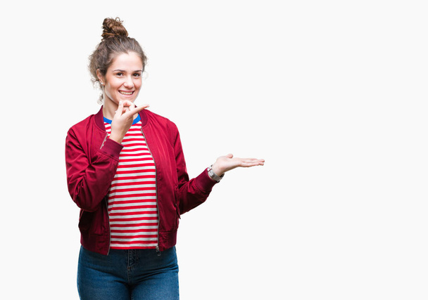 Beautiful brunette curly hair young girl wearing a jacket over isolated background amazed and smiling to the camera while presenting with hand and pointing with finger. - Photo, Image