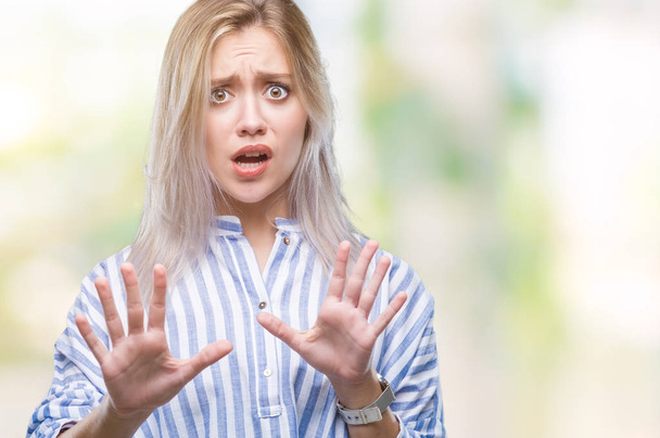 Young blonde woman over isolated background afraid and terrified with fear expression stop gesture with hands, shouting in shock. Panic concept. - Foto, imagen