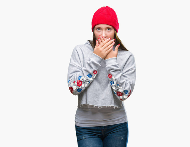 Young caucasian beautiful woman wearing wool cap over isolated background shocked covering mouth with hands for mistake. Secret concept. - Photo, Image