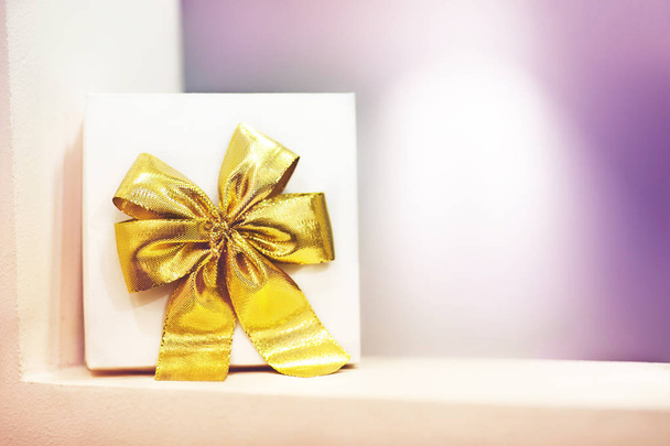 weiße Geschenkschachtel mit gelber Schleife steht im Regal auf violettem Hintergrund. Es gibt einen Platz für Text. - Foto, Bild