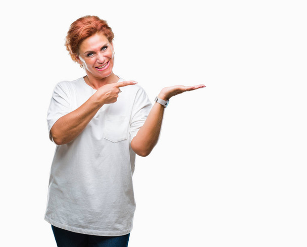Виступаюча старша біла руда жінка над ізольованим тлом здивована і посміхається камері, представляючи її рукою і вказуючи пальцем
. - Фото, зображення