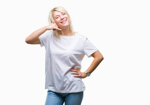 junge schöne blonde Frau trägt weißes T-Shirt über isoliertem Hintergrund und lächelt und macht Telefongesten mit Händen und Fingern, als spräche sie am Telefon. Vermittlung von Konzepten. - Foto, Bild