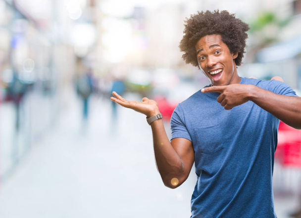 Afro amerykański człowiek na odosobnionym tle zdumiony i uśmiechnięty do kamery, prezentując się z ręką i wskazując palcem. - Zdjęcie, obraz