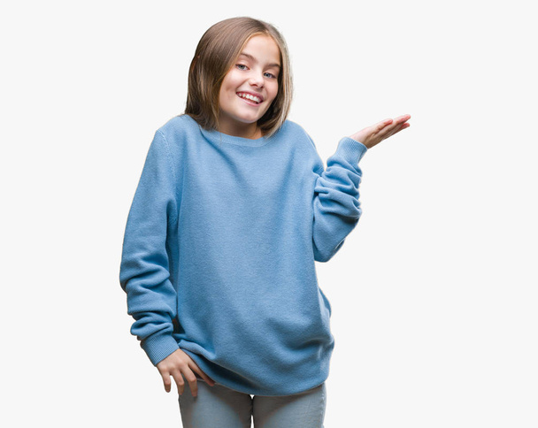 Young beautiful girl wearing winter sweater over isolated background smiling cheerful presenting and pointing with palm of hand looking at the camera. - Foto, imagen