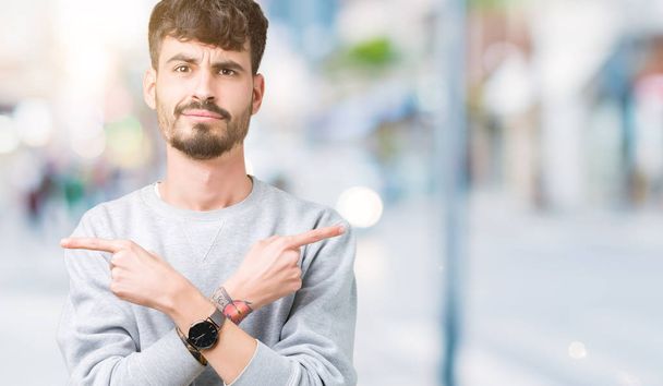 Young handsome man wearing sweatshirt over isolated background Pointing to both sides with fingers, different direction disagree - Фото, изображение