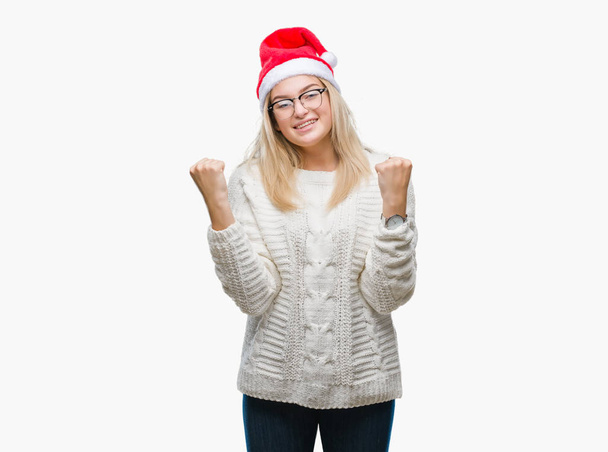 Giovane donna caucasica indossa cappello di Natale su sfondo isolato molto felice ed eccitato facendo gesto vincitore con le braccia alzate, sorridente e urlando per il successo. Concetto di celebrazione
. - Foto, immagini