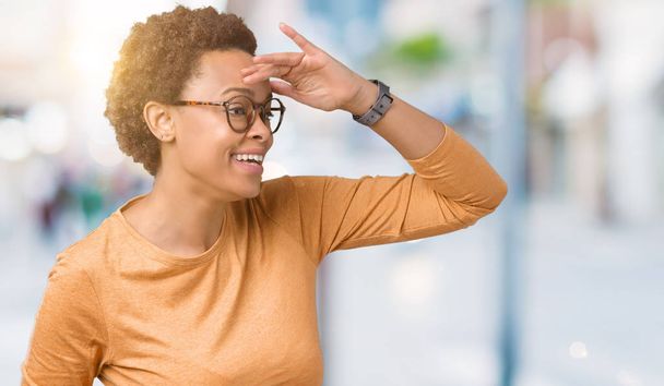 Giovane bella donna afroamericana indossa occhiali su sfondo isolato molto felice e sorridente guardando lontano con mano sopra la testa. Concetto di ricerca
. - Foto, immagini