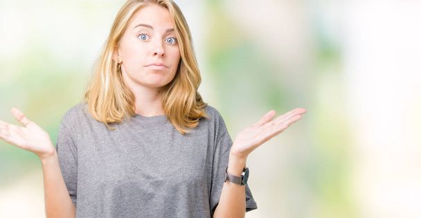 Beautiful young woman wearing oversize casual t-shirt over isolated background clueless and confused expression with arms and hands raised. Doubt concept. - Foto, Imagem