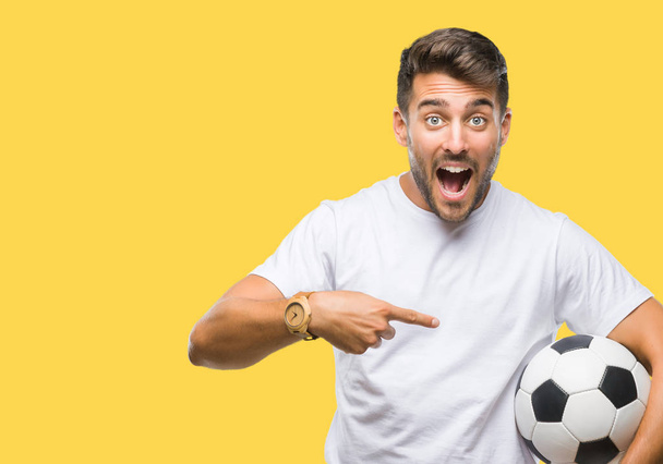 非常に幸せな手と指で指しての孤立した背景にサッカー サッカー ボールを保持している若いハンサムな男 - 写真・画像