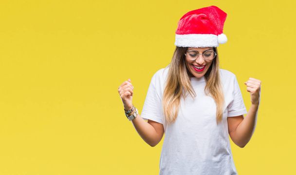 Giovane bella donna indossa cappello di Natale su sfondo isolato molto felice ed eccitato facendo gesto vincitore con le braccia alzate, sorridente e urlando per il successo. Concetto di celebrazione
. - Foto, immagini