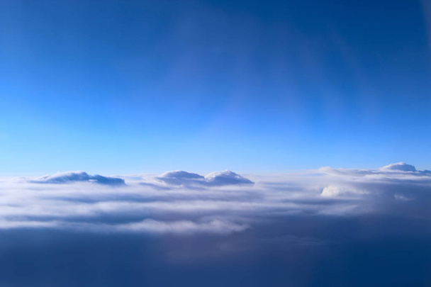 view from window of plane to white clouds. Unusual clouds illuminated by rays of sun. Beautiful white clouds on blue sky background. Landscape with sun and sky. Heaven panorama - Photo, Image