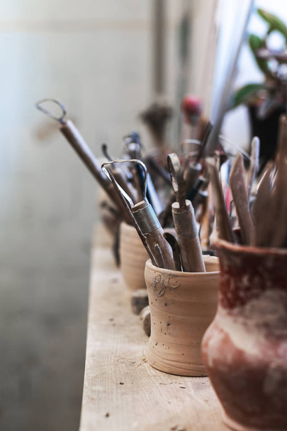Vertical close up photo of tools for ceramics work stand on window sill indoor workspace - Foto, imagen