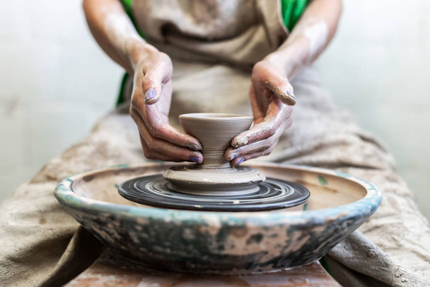 Recortada foto de cerca de la artesanía artista dama en su ropa de trabajo que se sienta dentro del espacio de trabajo hacer producto de cerámica para la venta por las manos
 - Foto, imagen