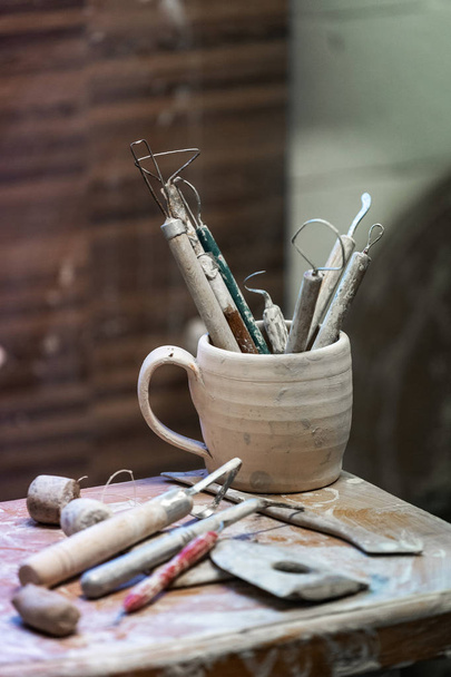 Vertical foto de cerca de las herramientas para el soporte de trabajo de cerámica en la vieja taza vintage en el espacio de trabajo interior de la mesa
 - Foto, Imagen