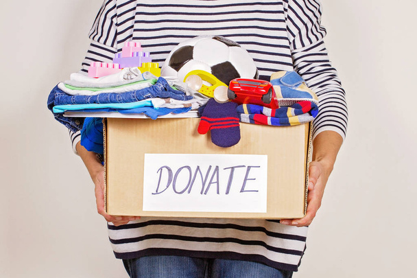 Женщина держит коробку для пожертвований с одеждой, игрушками и книгами для благотворительности
 - Фото, изображение
