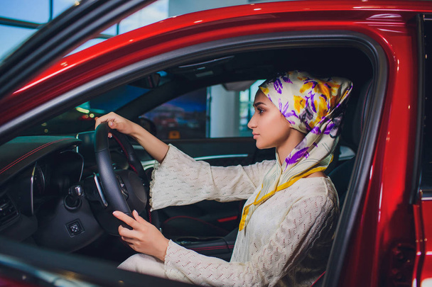 property and people concept - muslim woman in hijab with car key over car show background. happy woman taking car key from dealer in auto show or salon - Foto, immagini