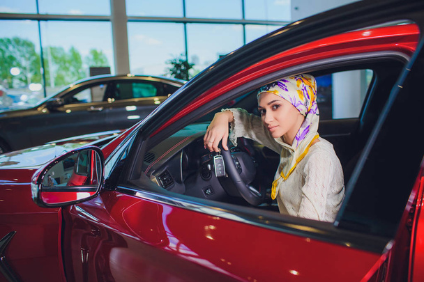 property and people concept - muslim woman in hijab with car key over car show background. happy woman taking car key from dealer in auto show or salon - Fotografie, Obrázek