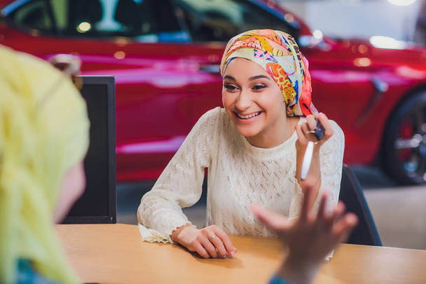 Beautiful woman enjoying happy moment getting car key from car seller auto salon. muslim woman in hijab - Foto, imagen