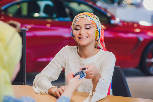 Beautiful woman enjoying happy moment getting car key from car seller auto salon. muslim woman in hijab - Фото, изображение