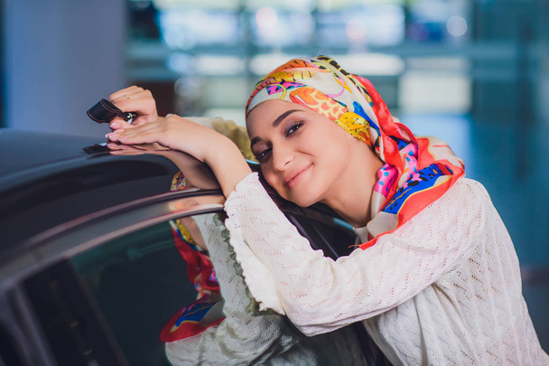 property and people concept - muslim woman in hijab with car key over car show background. happy woman taking car key from dealer in auto show or salon - Photo, Image