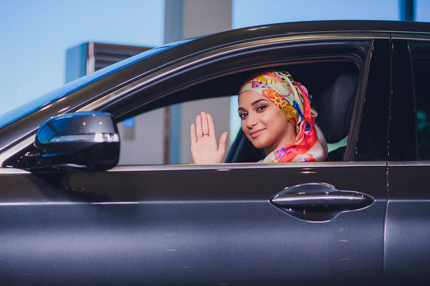 property and people concept - muslim woman in hijab with car key over car show background. happy woman taking car key from dealer in auto show or salon - Φωτογραφία, εικόνα