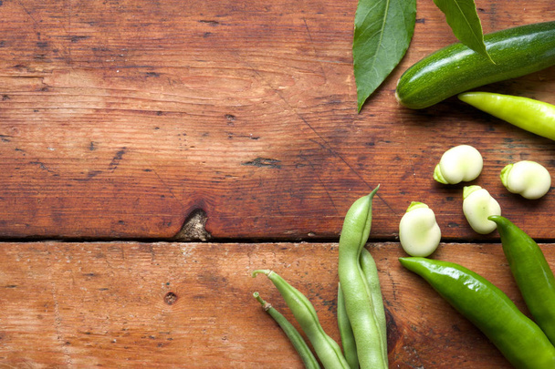 green beans, broad beans clove leaves and green chilli on a rustic wooden table top, the vegetables are arranged on the right side of the image leaving space on the right side of the chopping board for copy space, still life, horizontal format - Photo, Image