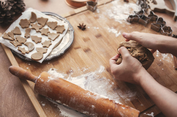 Handen kneden van deeg voor peperkoek cookies op rustieke tafel op achtergrond van houten deegroller, koekjes, metalen scharen, kerstversiering. Sfeervolle afbeelding. - Foto, afbeelding