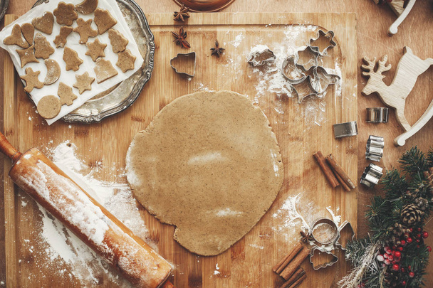 Dough with metal cutters on rustic table with wooden rolling pin, cinnamon ,anise, cones, christmas decorations, flat lay . Making christmas cookies, atmospheric image - Foto, afbeelding