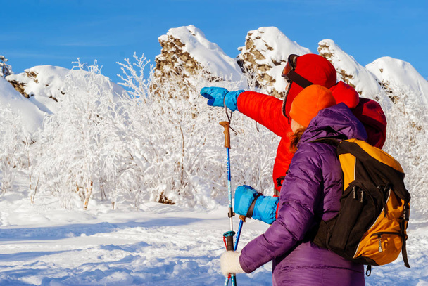 muž a žena cestovatele v zimních horách podívat do vzdálenosti opodál zasněžené skály za slunečného mrazivého dne - Fotografie, Obrázek