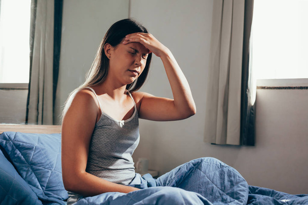 Young woman with headache sitting on her bed - Photo, image